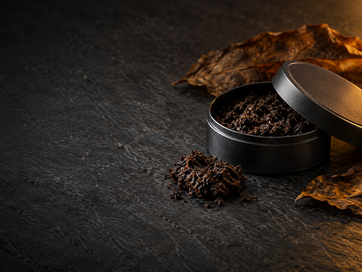 Open black tin of loose dark snus with dried tobacco leaves